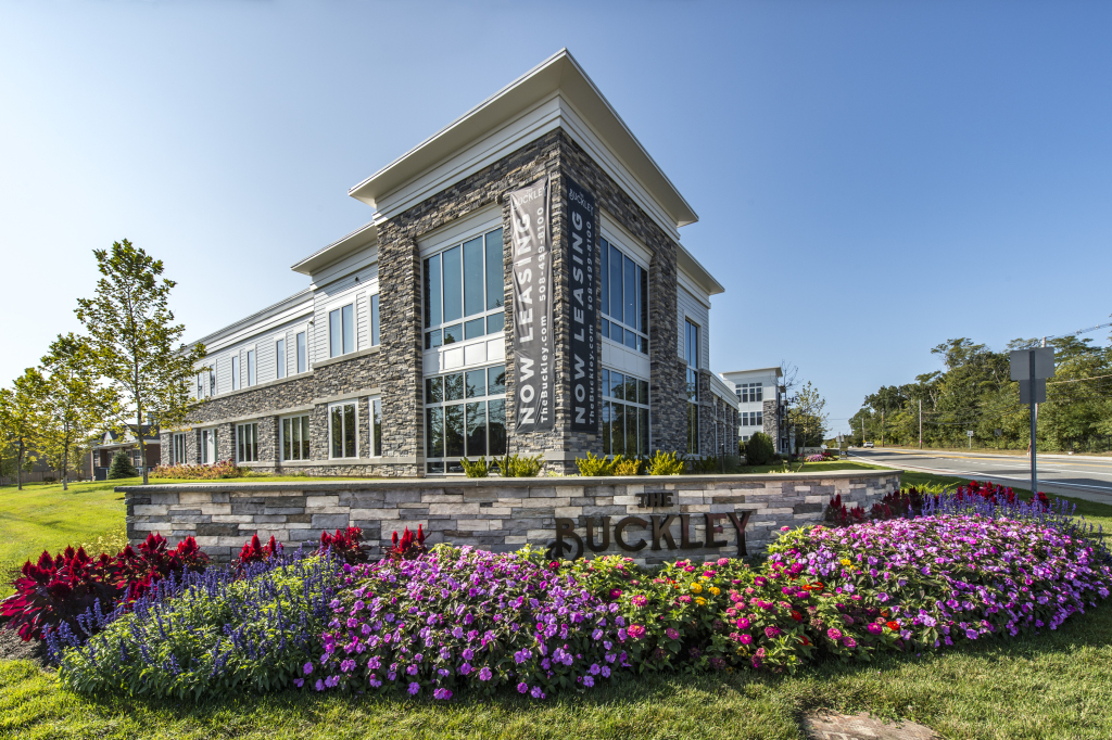 Modern Buckley office building with stone facade and glass windows, surrounded by colorful flower gardens and landscaping