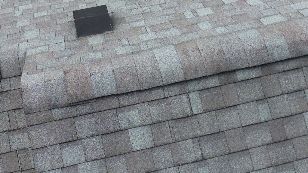 Asphalt shingle roof with black vent pipe protruding from gray weathered shingles in overlapping rows