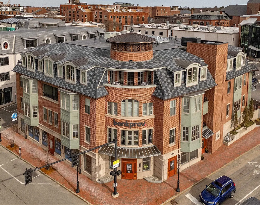 Aerial view of curved brick apartment building with distinctive round tower and slate roof on corner of urban street intersection