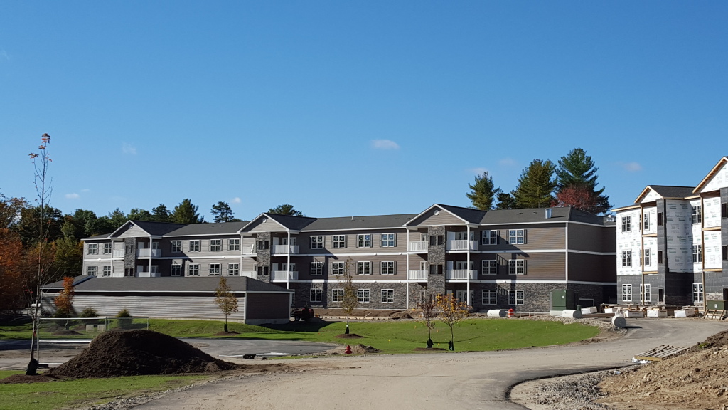 Multi-story apartment complex under construction with stone and siding exterior, surrounded by trees and construction materials