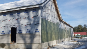 House under construction with Typar house wrap and green siding partially installed on concrete foundation in winter