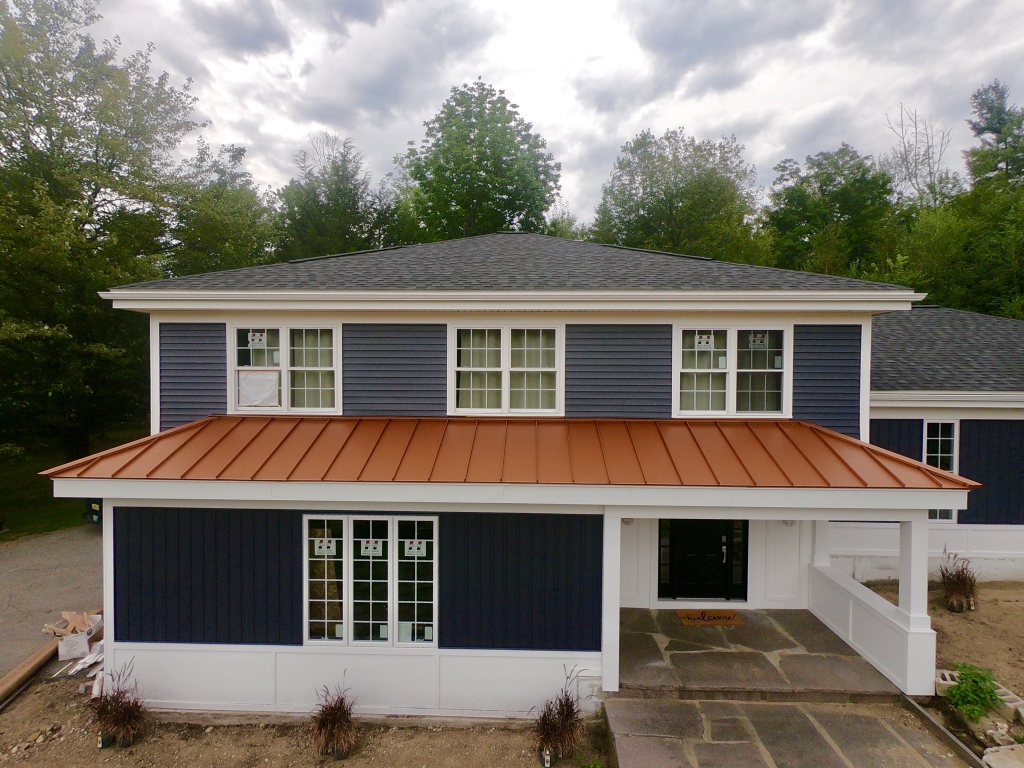 Modern two-story house with blue siding, copper metal roof, white trim, and covered patio surrounded by trees
