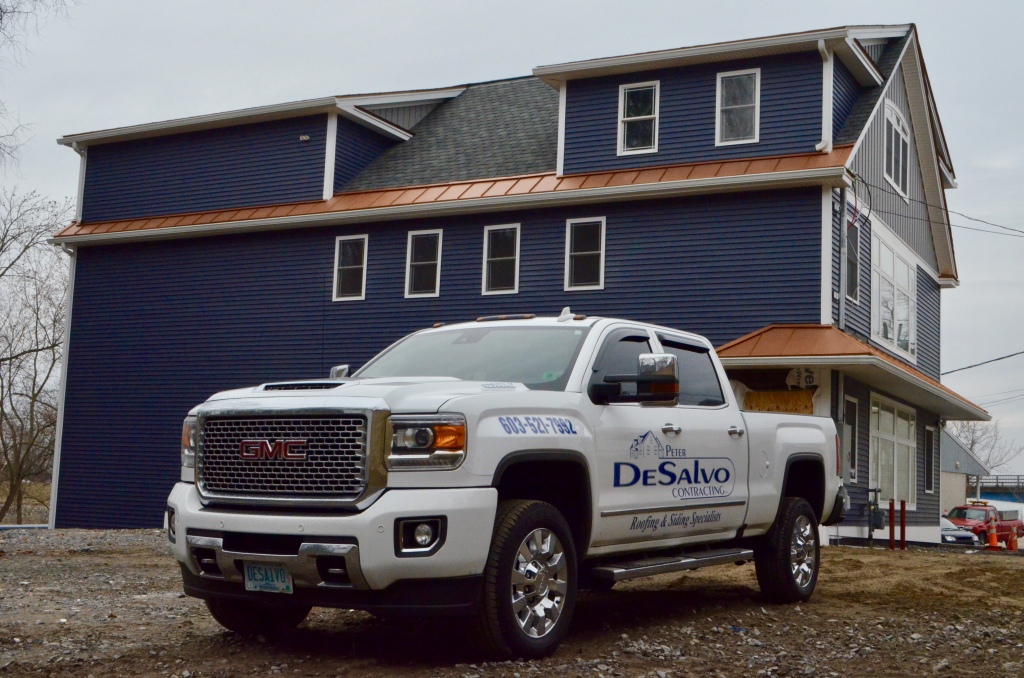White GMC pickup truck with DeSalvo Contracting logo parked in front of blue two-story house under construction