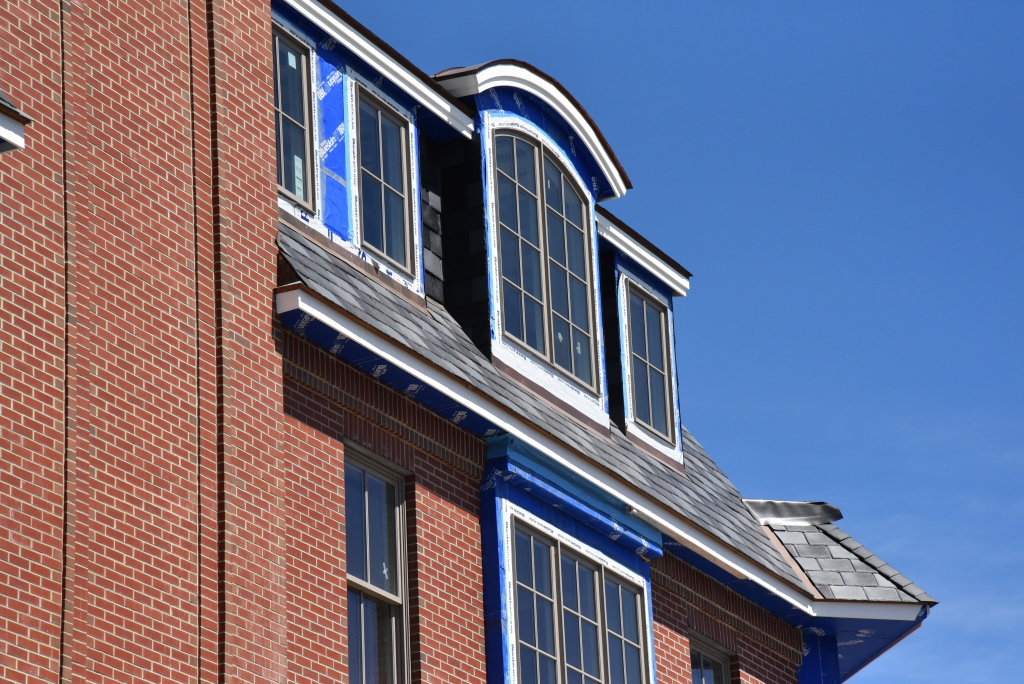 Red brick building with blue trim and curved dormer windows against clear blue sky, showing architectural detail of residential structure