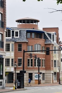 Modern brick building with distinctive circular tower and blue slate roof in downtown area with traffic lights and street view