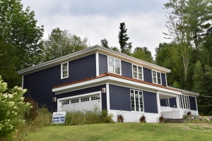 Two-story colonial home with navy blue siding, white trim, and copper accents surrounded by lush green trees