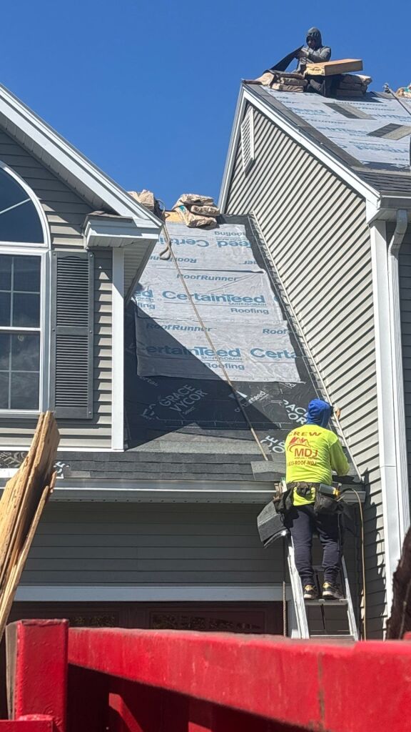 Roofing contractors installing CertainTeed roofing materials on residential house with worker on ladder and another on roof