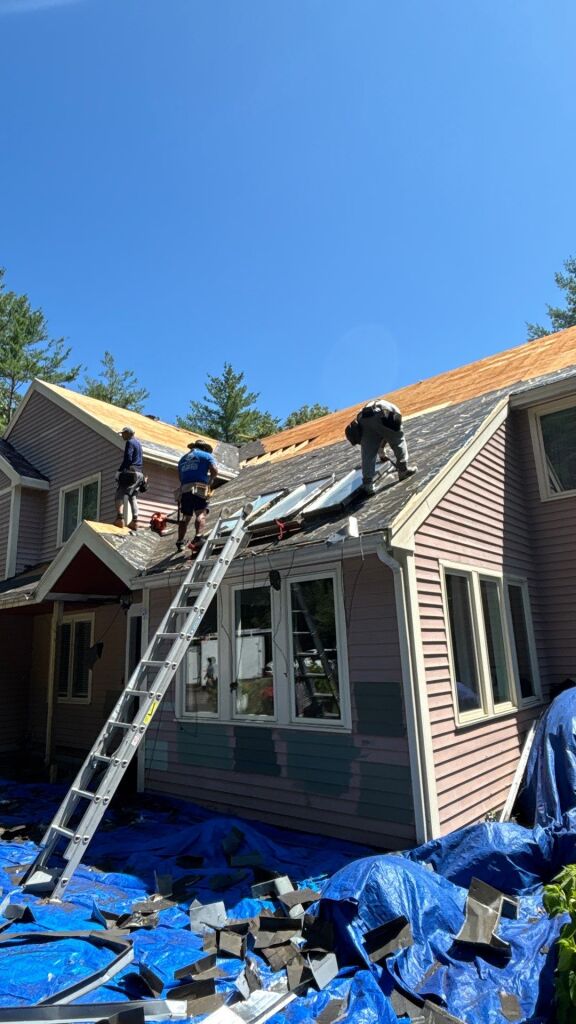 Roofers working on residential home roof replacement with ladder, blue tarps covering old shingles on sunny day