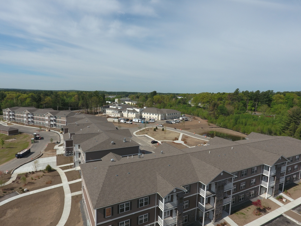 Aerial view of modern apartment complex under construction with multiple residential buildings, paved walkways, and surrounding forest