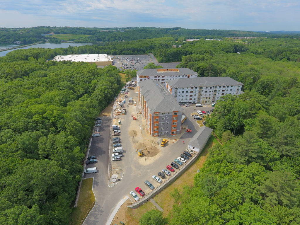 Aerial view of apartment complex construction site with completed buildings, active construction area, and surrounding forest