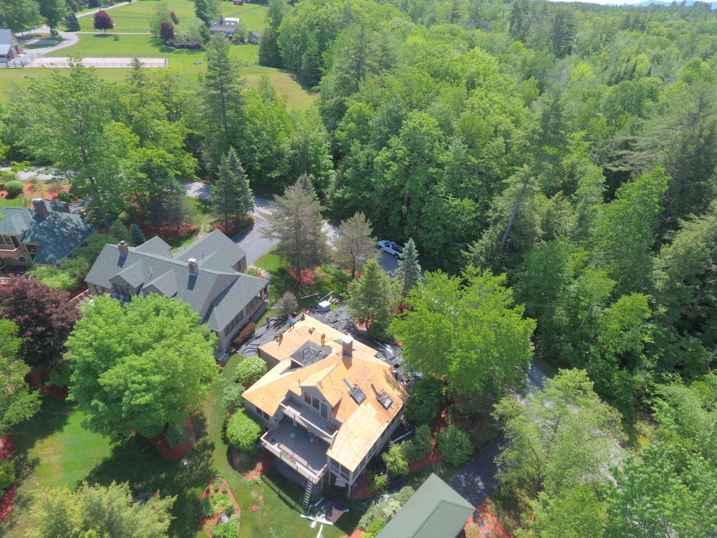 Aerial view of residential home with new wooden roof construction surrounded by lush green trees in suburban neighborhood