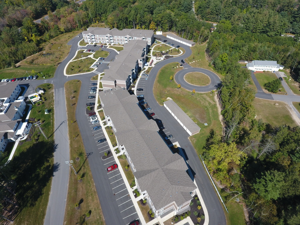 Aerial view of modern healthcare facility with curved architecture, extensive parking, and landscaped grounds surrounded by forest