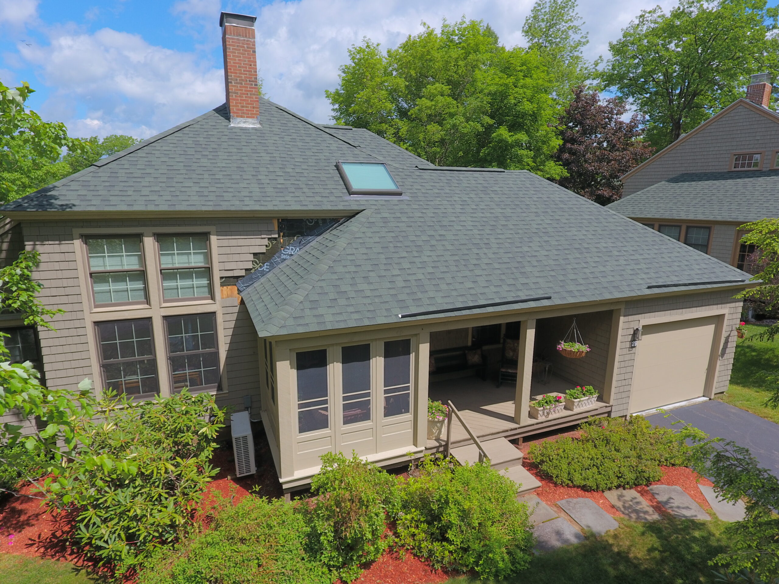 Aerial view of a modern single-story home with gray shingles, covered porch, skylights, and landscaped yard with red mulch