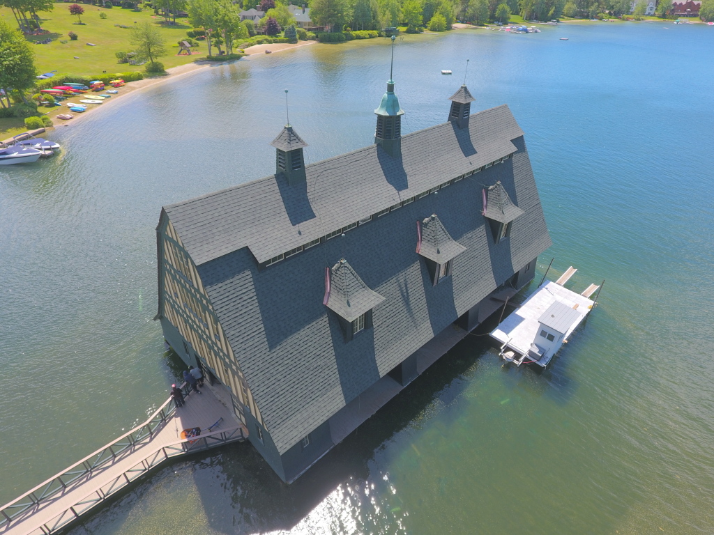 Aerial view of historic wooden building on stilts over lake water with multiple spires and dormers, connected by wooden walkway