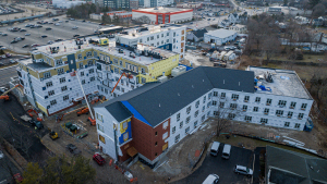 Aerial view of large multi-story apartment complex under construction with cranes, scaffolding, and construction equipment visible