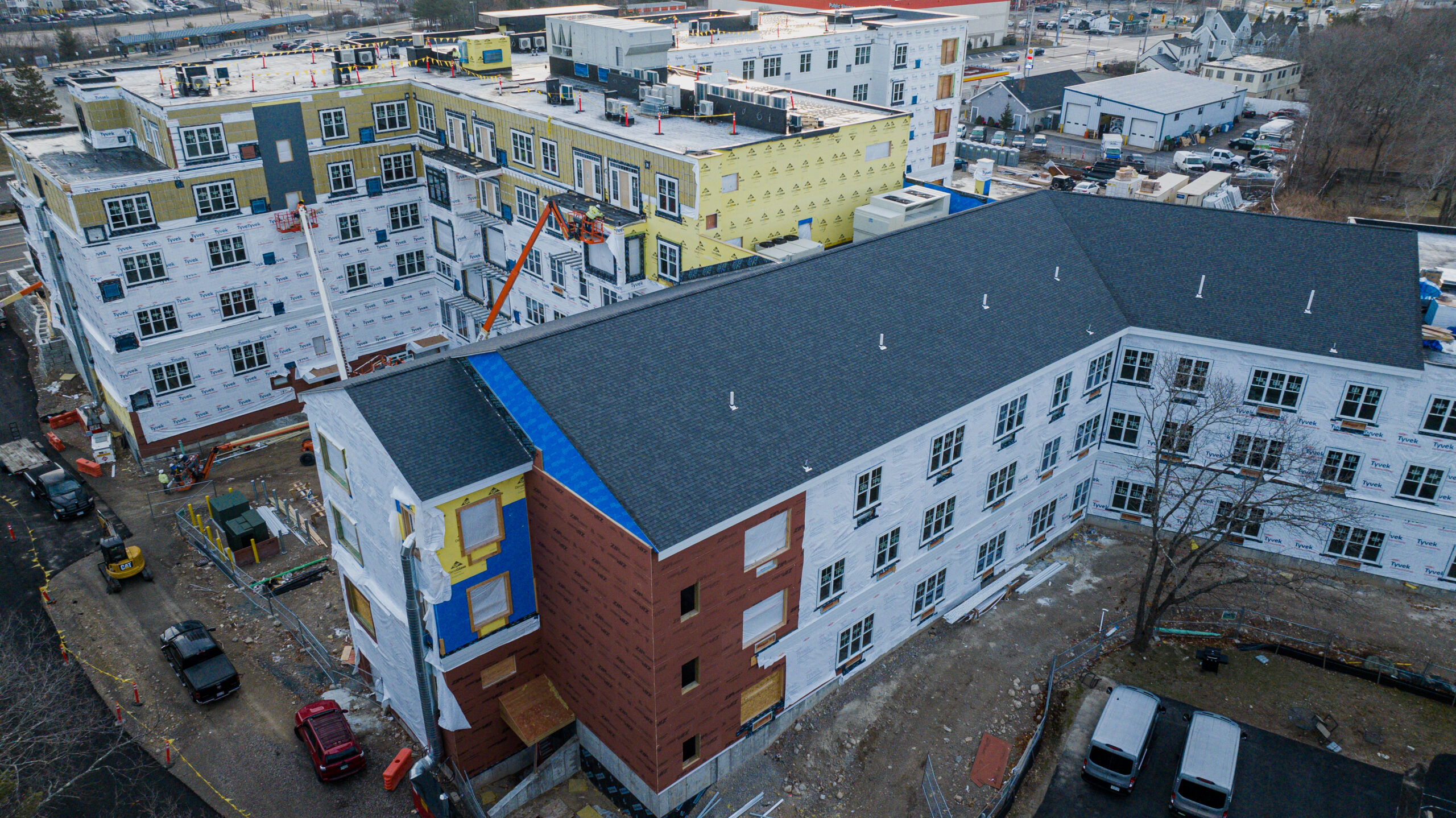 Aerial view of multi-story residential buildings under construction with dark roofing, colorful siding, and construction equipment nearby
