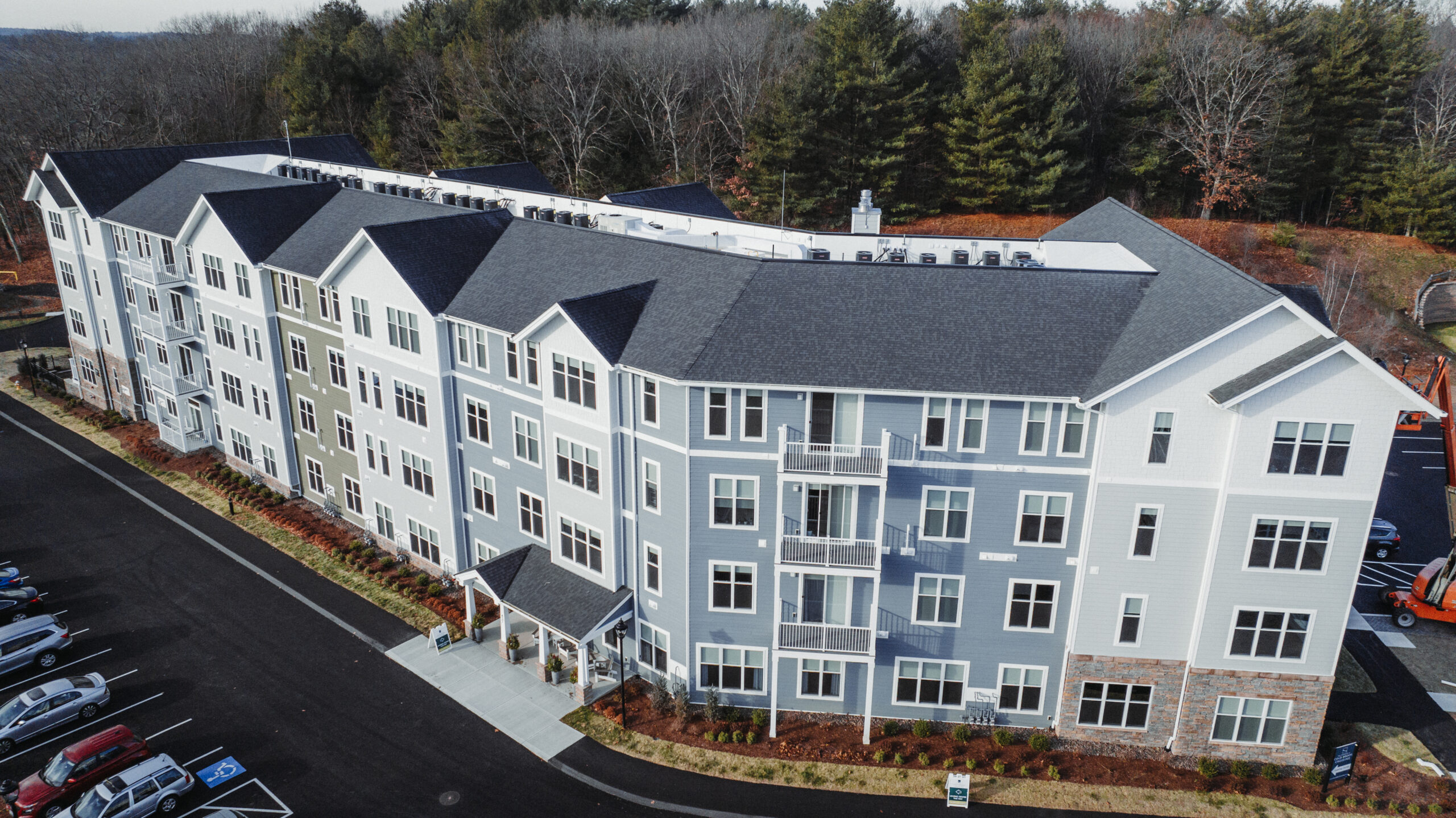 Modern multi-story apartment complex with gray siding, dark roofs, and balconies surrounded by trees and parking lot