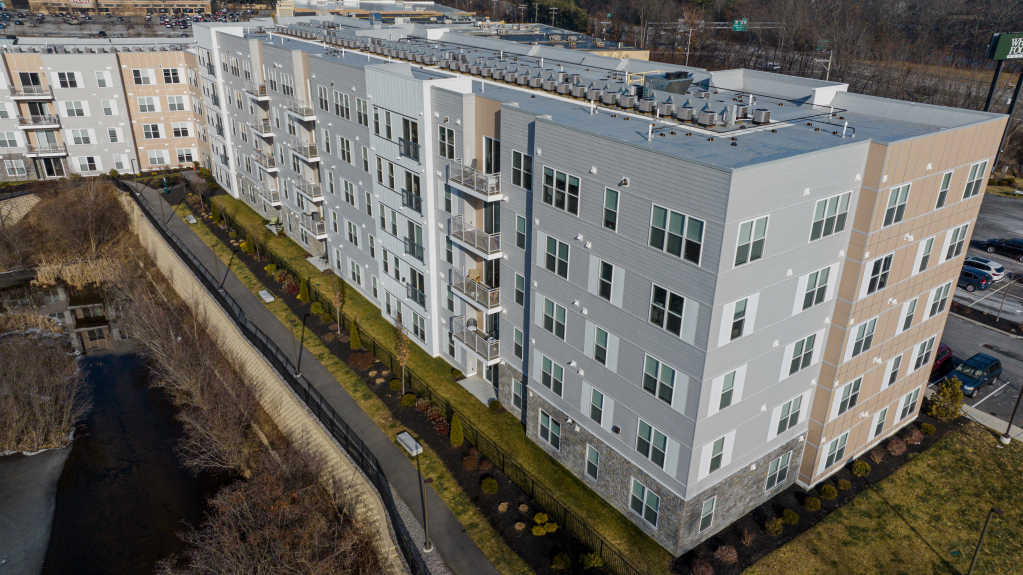 Aerial view of modern multi-story apartment complex with white and beige exterior, landscaped grounds, and parking areas
