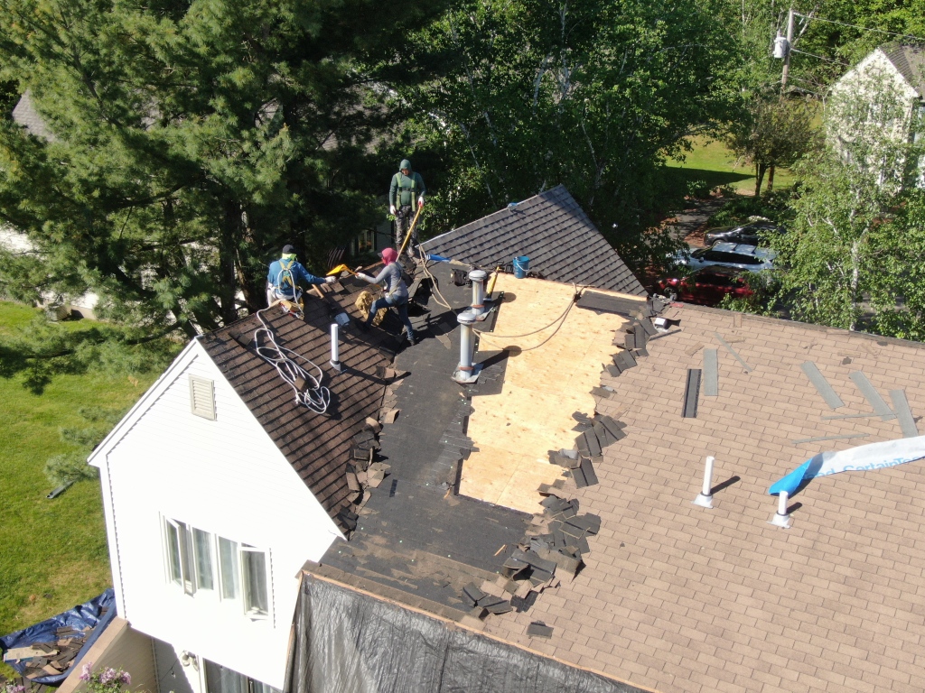 Aerial view of roofers working on residential home roof repair, removing damaged shingles and installing new plywood decking