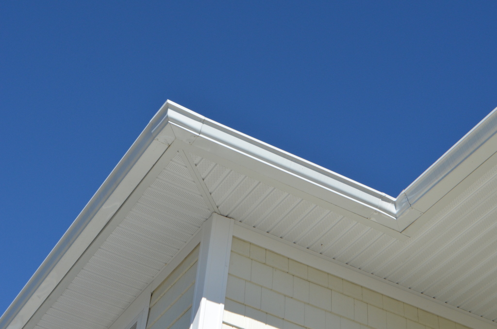 White house exterior corner showing roof eaves, soffits, and siding against bright blue sky - residential architecture detail