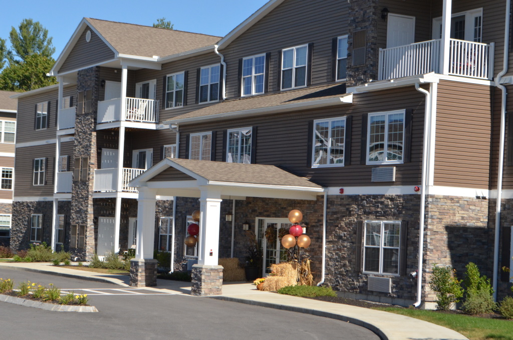 Modern multi-story apartment building with stone and vinyl siding, white balconies, and fall decorations at entrance