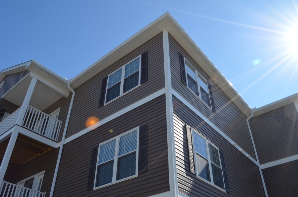 Modern two-story residential building with brown vinyl siding, white trim, and multiple windows under clear blue sky