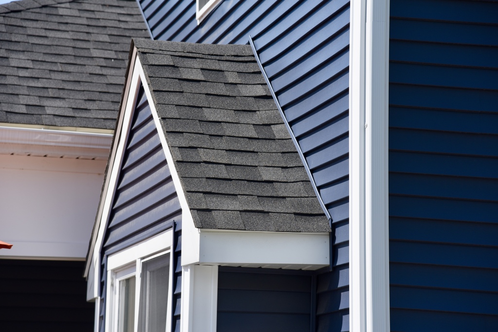 Modern house exterior showing asphalt shingle roof, white vinyl siding, and blue siding with white trim around windows