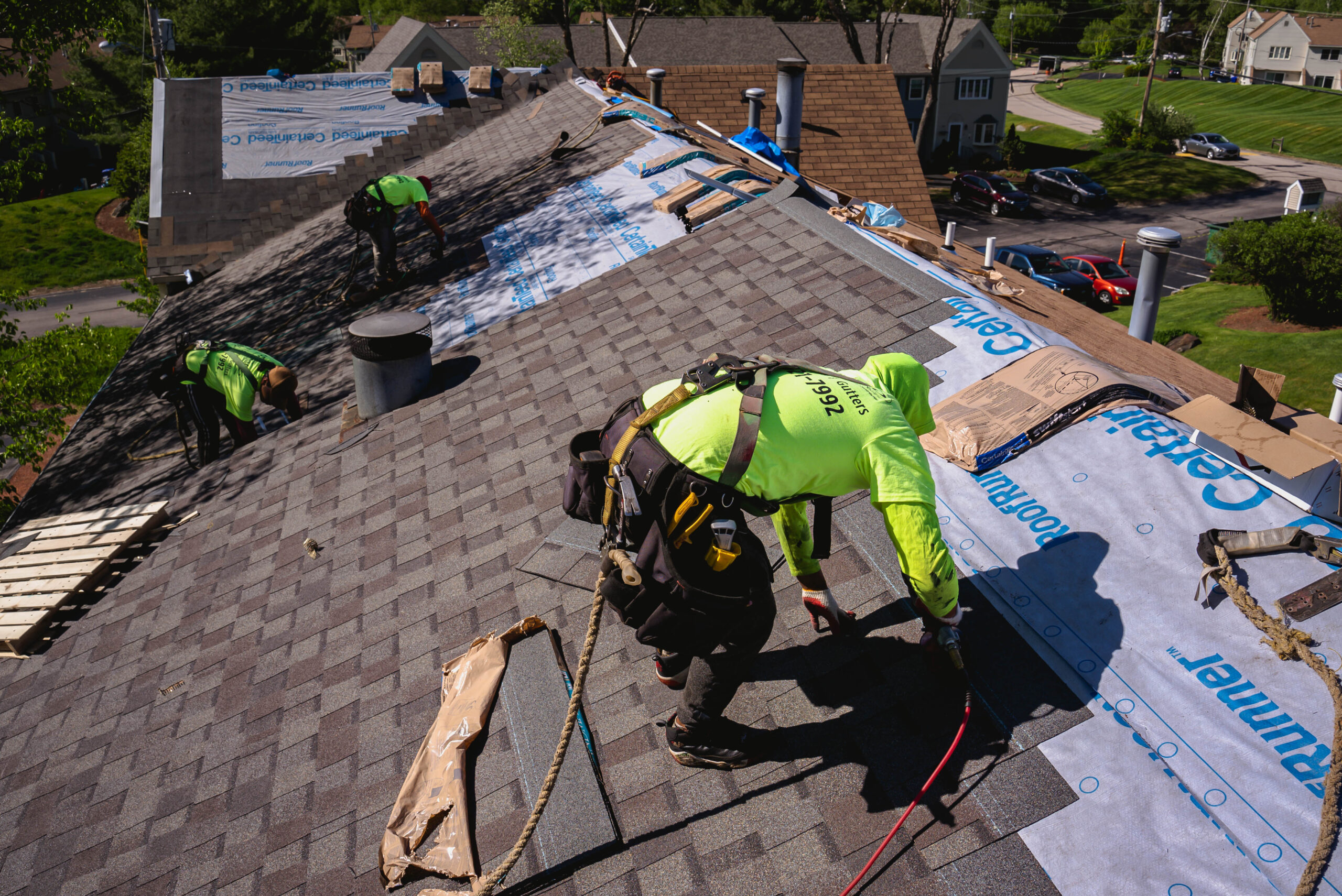 Roofing contractors in high-visibility safety vests installing shingles on residential house roof with underlayment visible