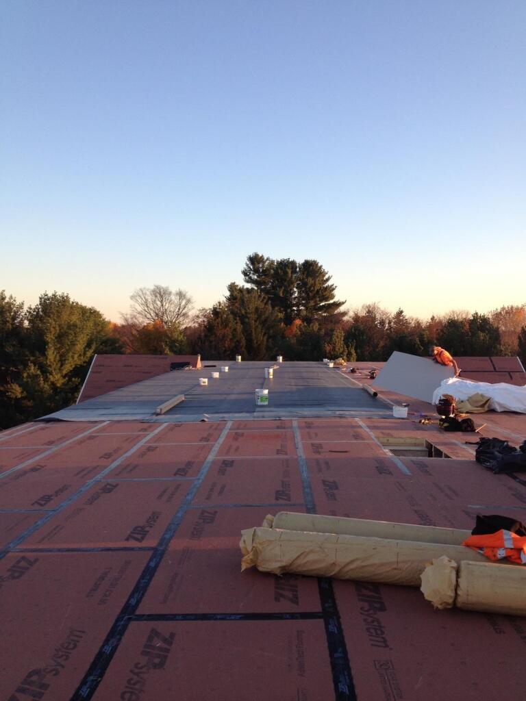 Roofing construction work in progress showing pink insulation boards being installed on commercial building roof at dusk