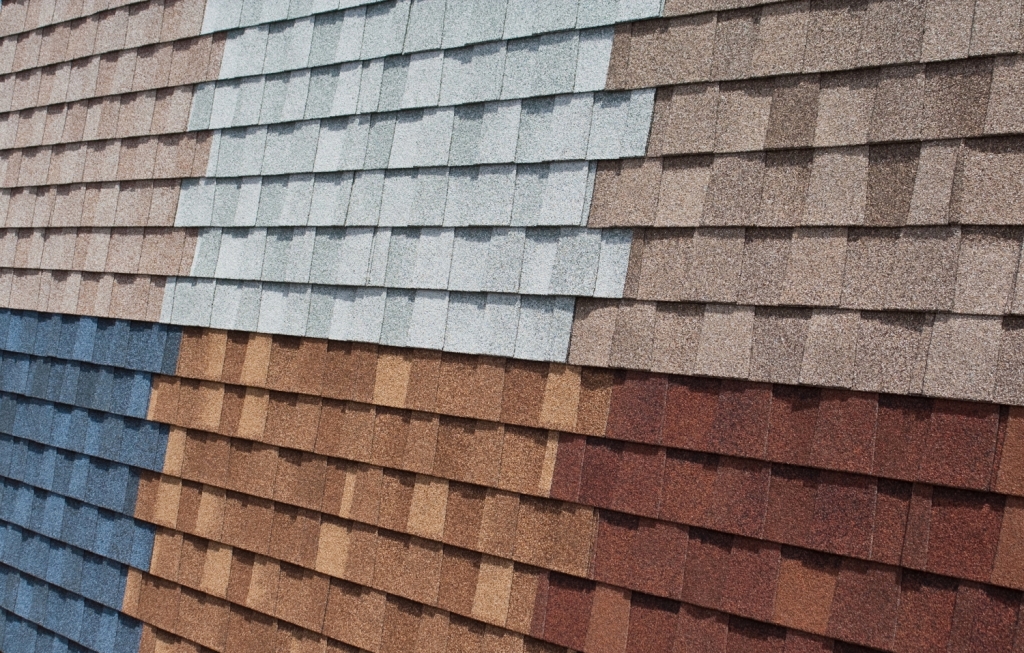 Display of colorful asphalt roof shingles in various shades including blue, brown, gray, and red arranged in overlapping rows