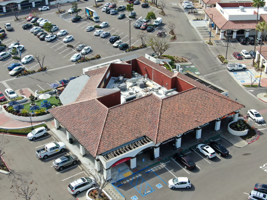 Aerial view of Spanish-style commercial building with red tile roof and white columns in shopping center parking lot