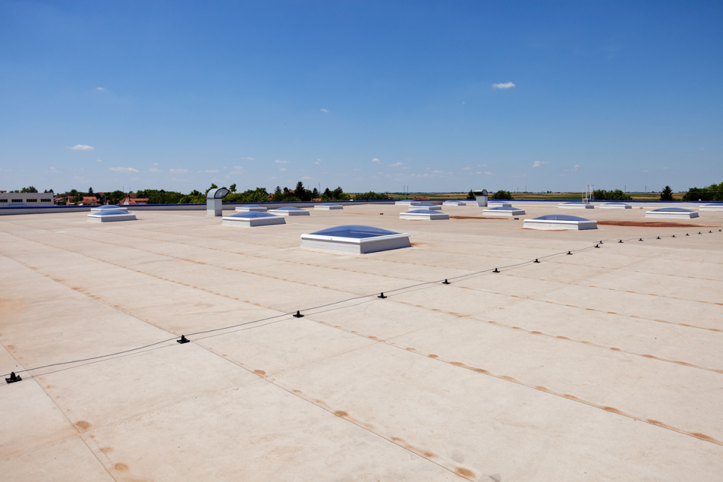 White commercial flat roof with multiple skylights and ventilation units under clear blue sky with residential buildings in background
