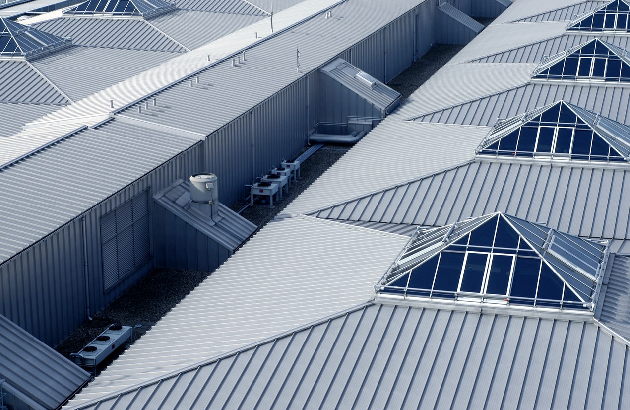 Aerial view of modern industrial building with corrugated metal roofing, geometric skylights, and HVAC equipment on rooftop