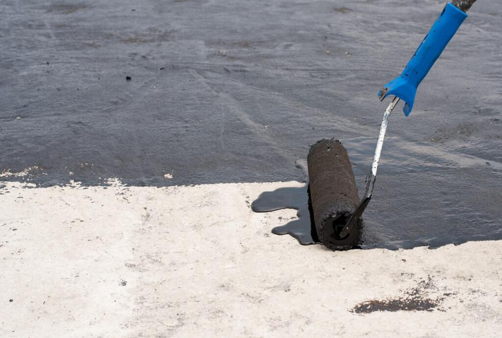 Person in blue gloves using shovel to dig black sand or sediment sample at beach water's edge for environmental testing or research