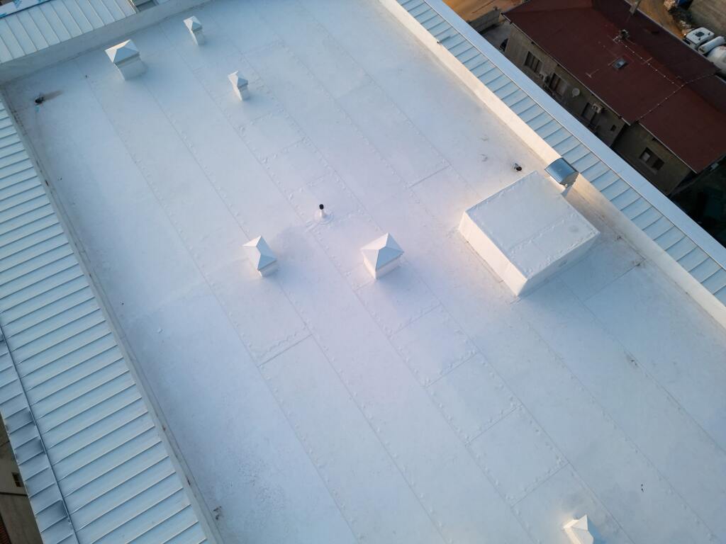 Aerial view of white commercial flat roof with metal ridged edges and ventilation units, showing clean membrane surface
