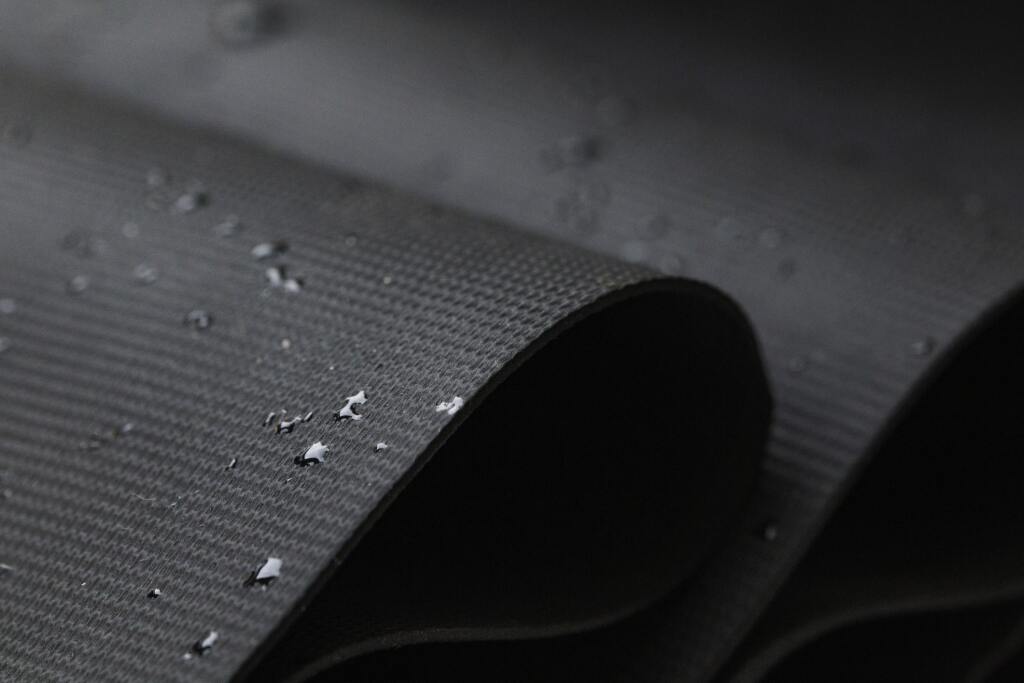 Close-up of water droplets beading on dark waterproof fabric surface, showing hydrophobic textile properties