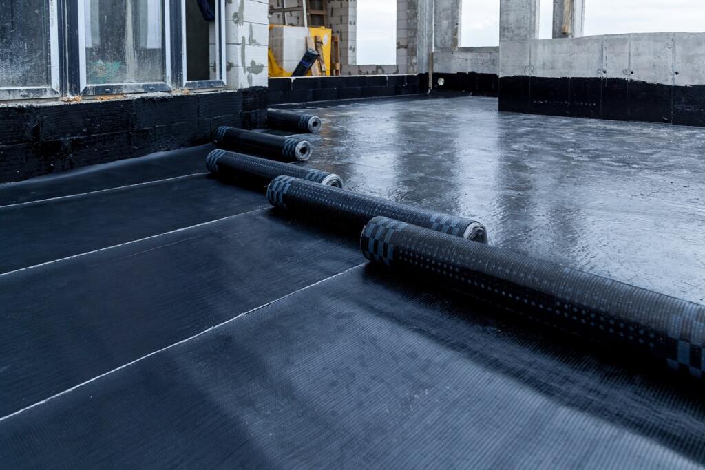 Black waterproof membrane rolls being installed on concrete floor during construction waterproofing process