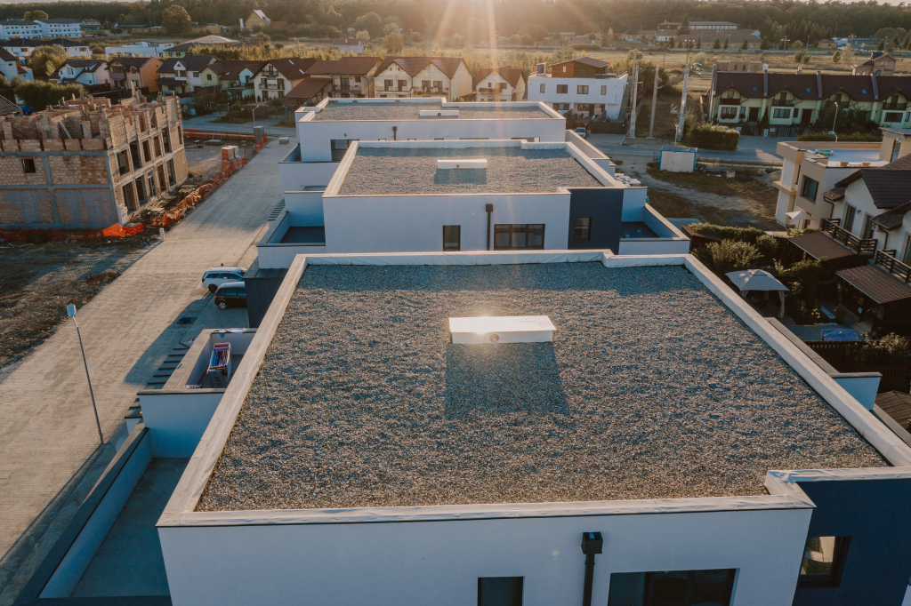 Aerial view of modern white flat-roof building with gravel rooftop in residential neighborhood during golden hour sunset