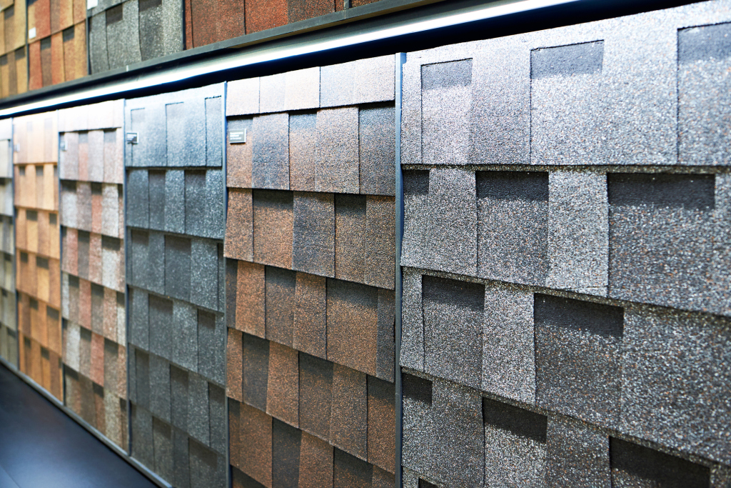 Display of various asphalt roofing shingle samples in different colors and textures arranged on shelves in a showroom