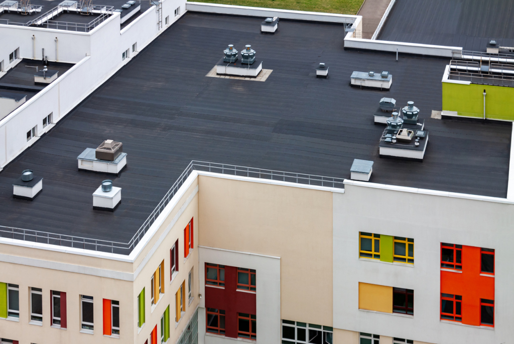 Aerial view of modern commercial building rooftop with HVAC equipment, dark membrane roof, and colorful window panels in orange, yellow, green
