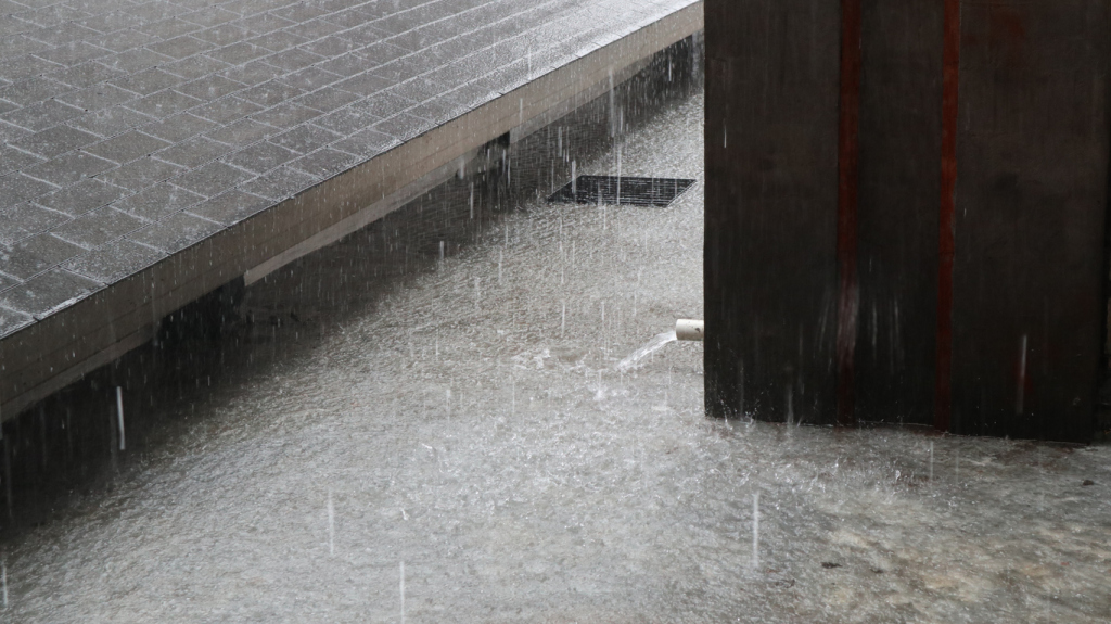 Heavy rain flooding an underground parking garage or tunnel with water cascading from ceiling and pooling on concrete floor