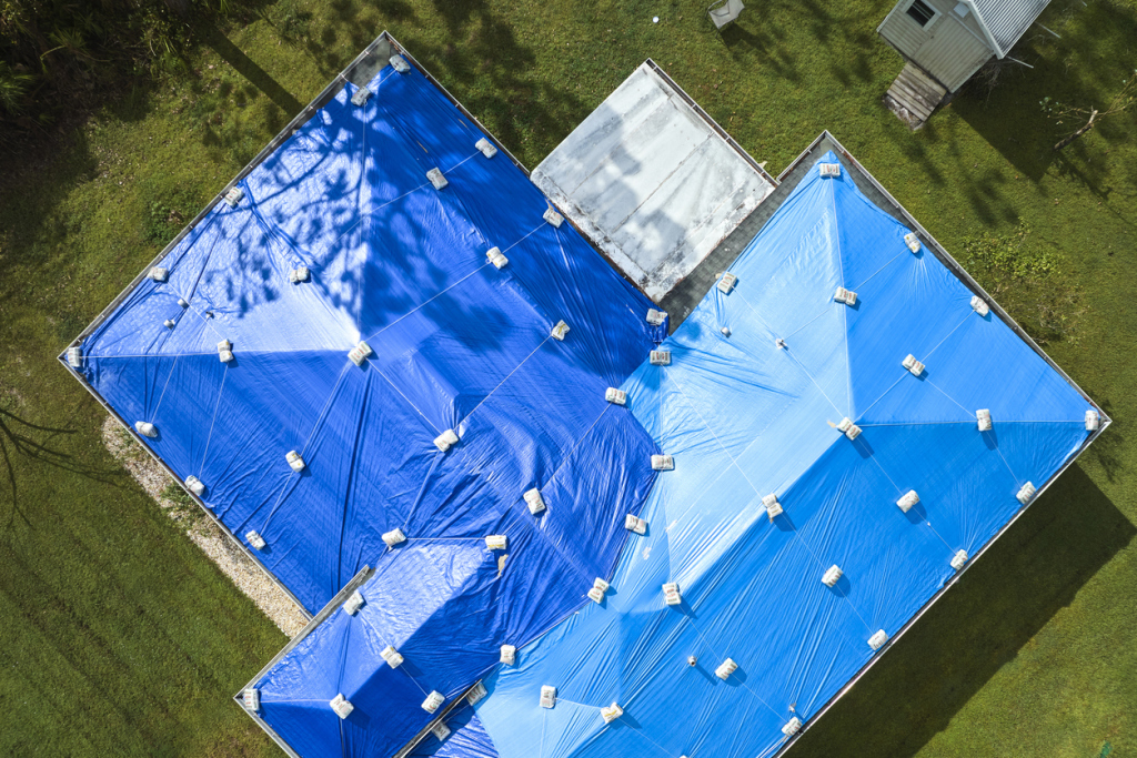 Aerial view of blue tarps covering building roofs with white anchor points, surrounded by green grass and utility buildings