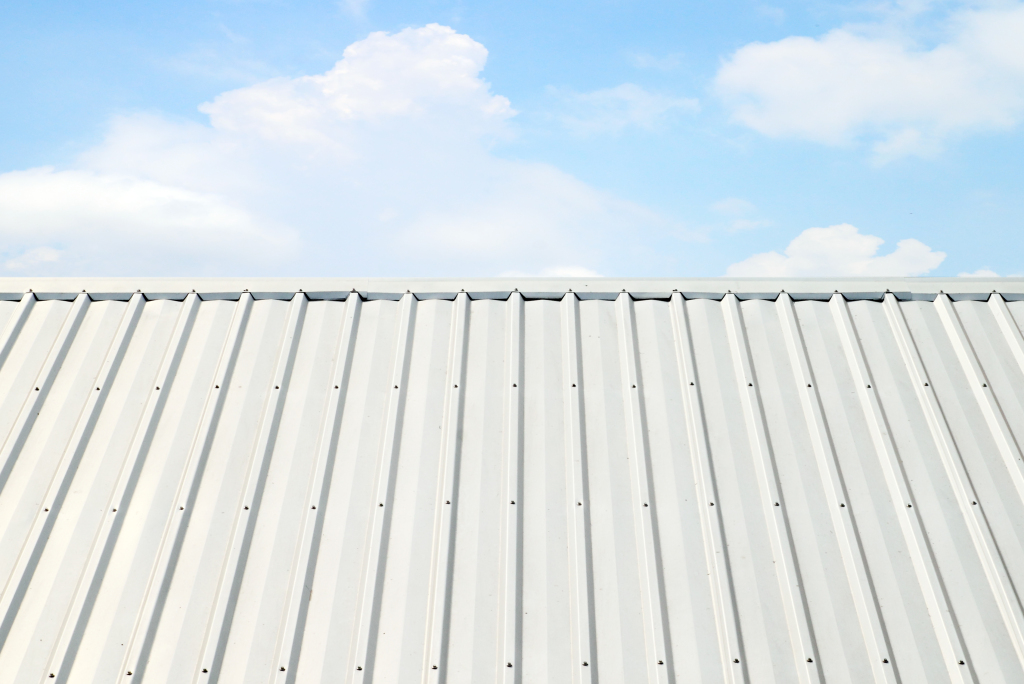 White corrugated metal roof with vertical ridges against blue sky with white clouds