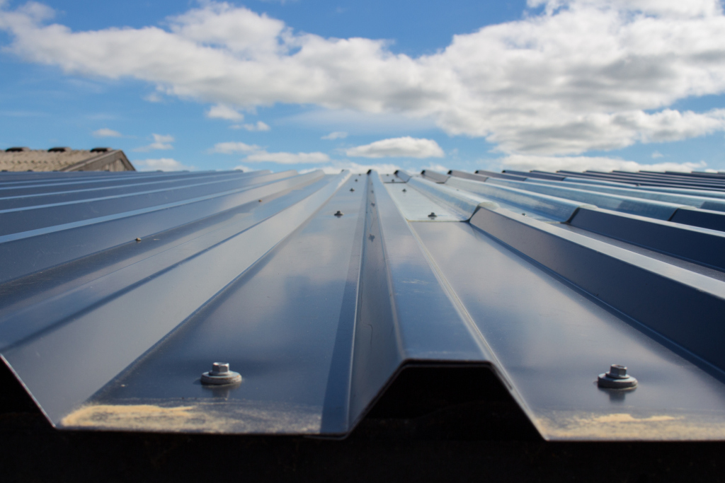 Metal roofing panels with standing seam construction extending toward horizon under blue sky with white clouds