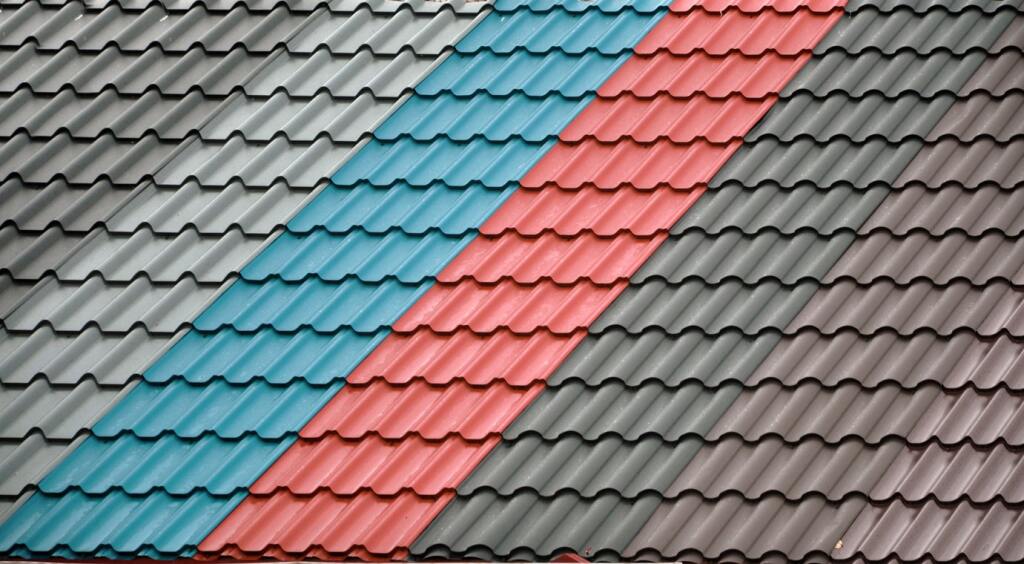 Colorful metal roof tiles in blue, red, and gray arranged in overlapping rows, showing different roofing material options