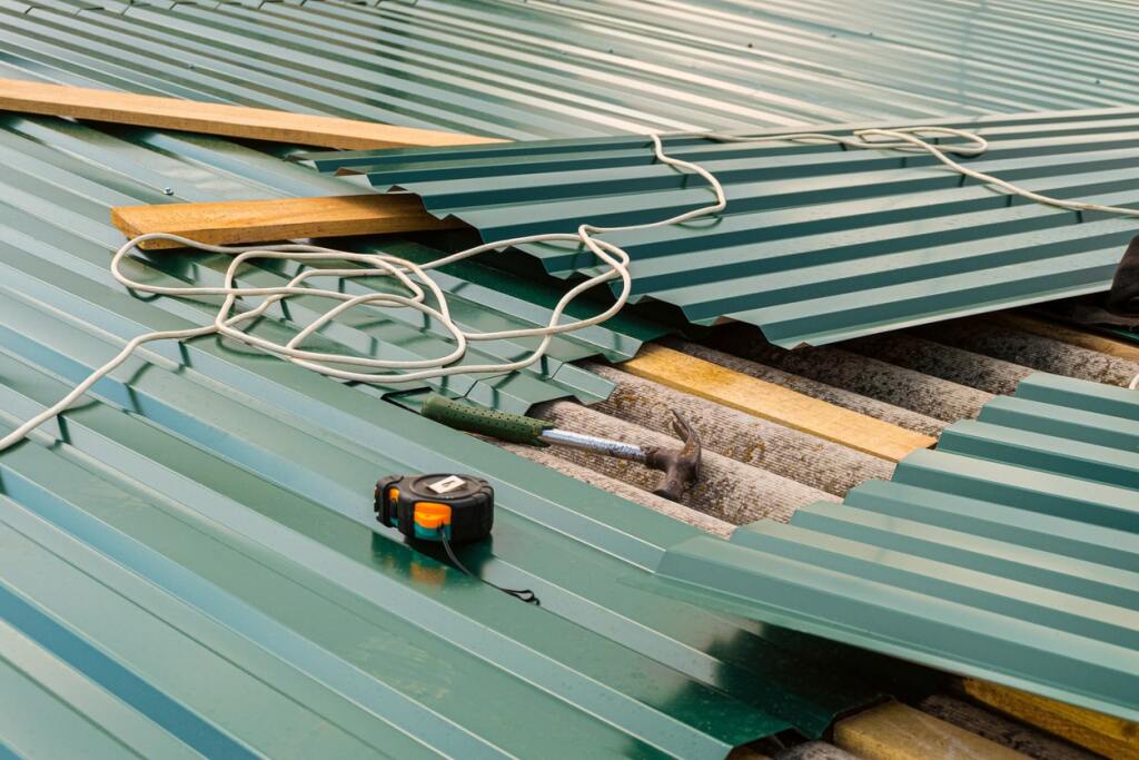 Green metal roofing sheets with wooden battens, measuring tape, and white electrical cables during construction installation