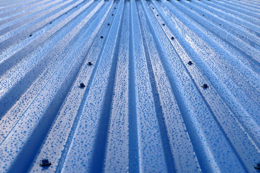 Blue metal roof with corrugated ridges and water droplets creating a perspective view with linear pattern extending to horizon