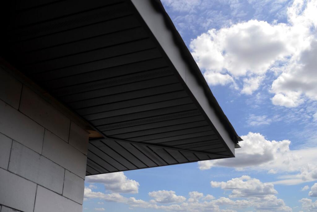 Modern building exterior with angular overhang and horizontal siding against blue sky with white clouds