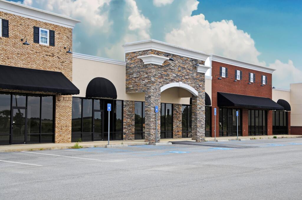 Modern commercial strip mall with brick, stone and stucco facades, black awnings, large windows and parking spaces in front