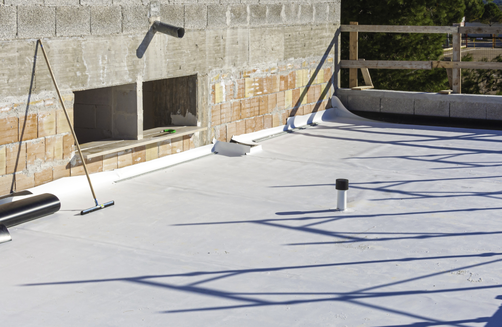 Flat roof construction site with white membrane, concrete blocks, wooden framework, and construction equipment during building work